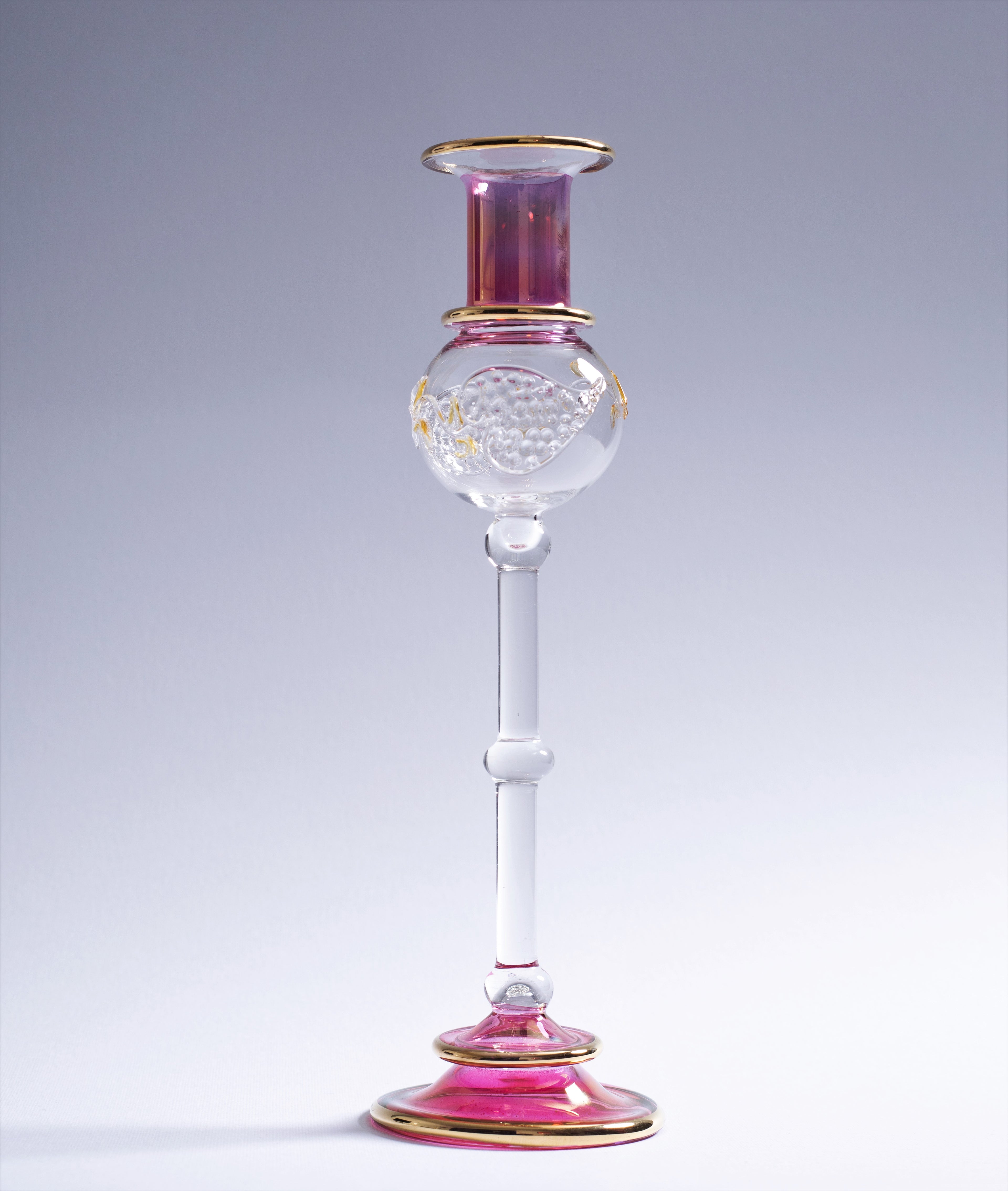 Decorative glass candlestick with pink and gold accents on a gray background