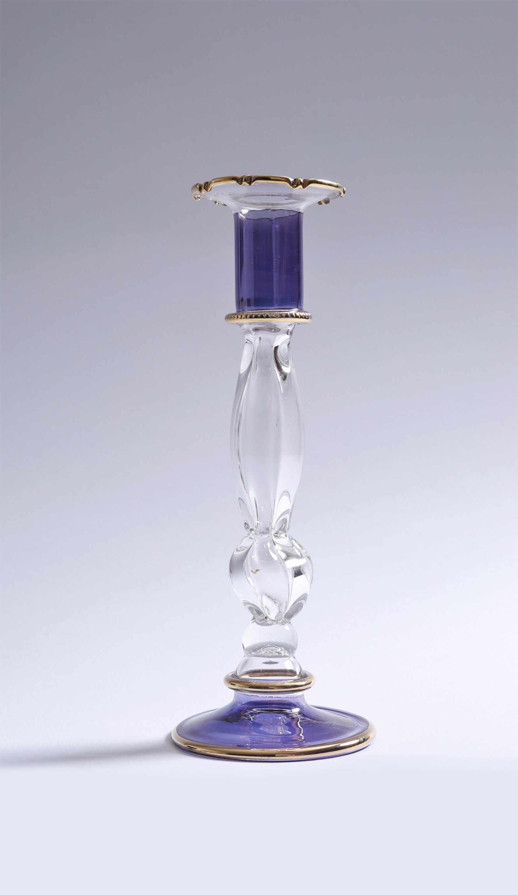 Decorative glass candlestick with a purple candle on a gray background