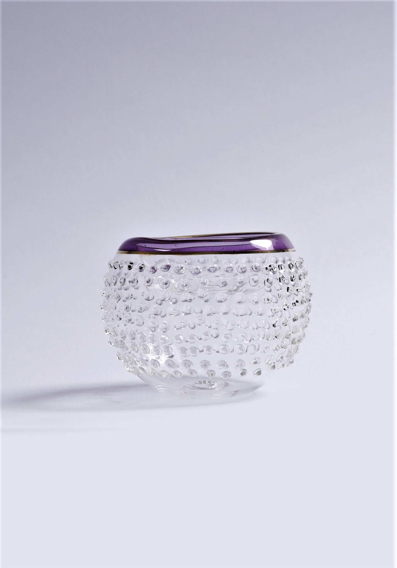 Clear glass vase with textured design and purple rim on a light gray background