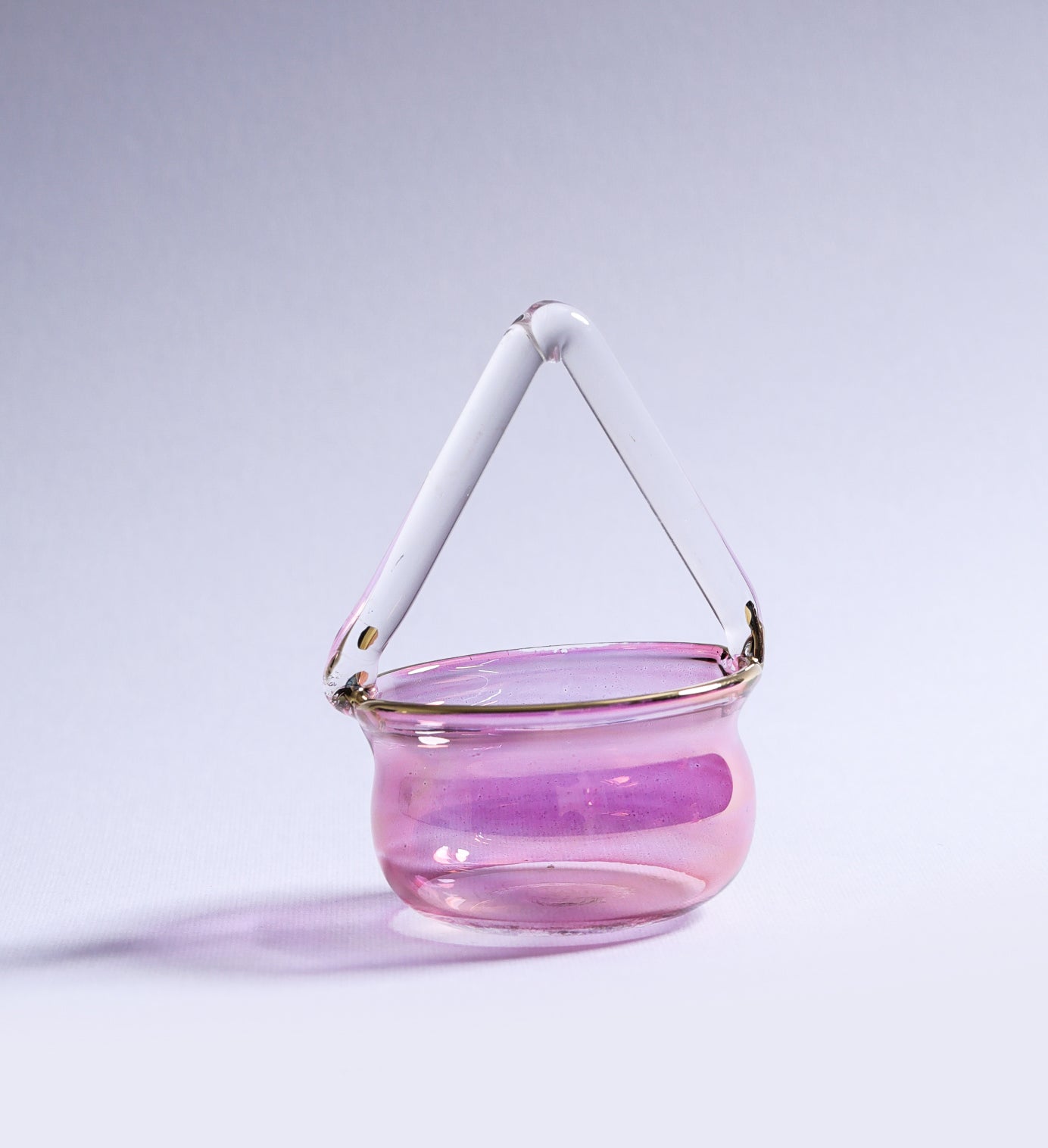 Pink glass basket with a white handle on a light purple background