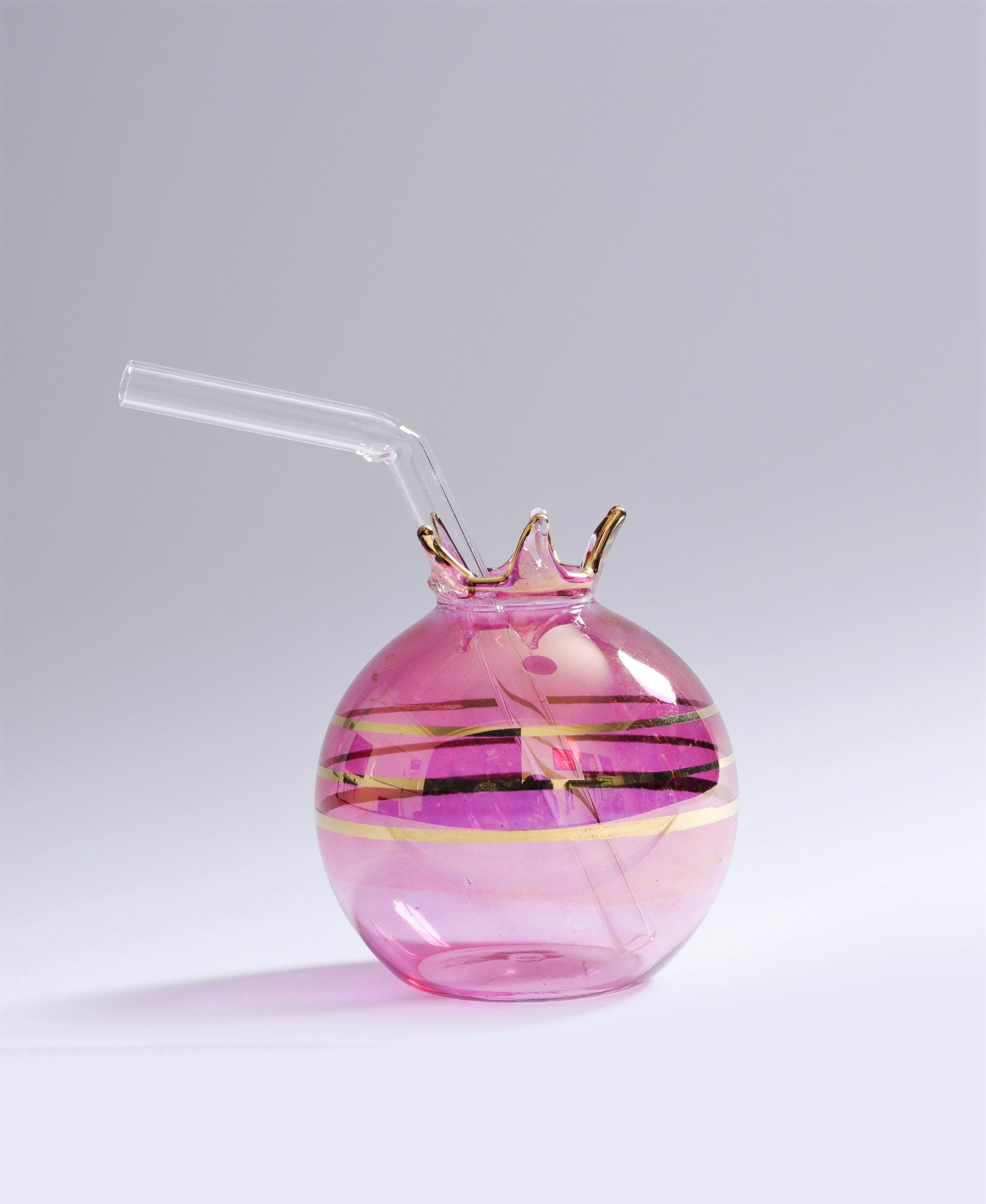 Pink glass drink container with gold accents and a straw on a light gray background