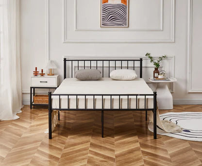 Bedroom with a black metal bed frame, white mattress, and decorative items on a wooden floor.