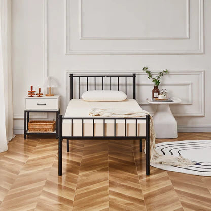 Bedroom with a black metal bed frame, white bedding, and decorative items on a wooden floor.
