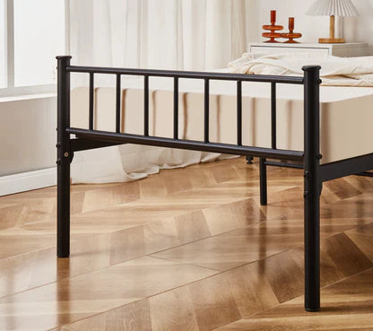 Black metal bed frame on a wooden floor with a neutral-colored wall and window in the background.