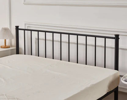 Black metal bed frame with white mattress against a white wall.
