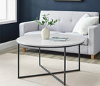 Round coffee table with a vase and books in front of a gray sofa against a blue wall.
