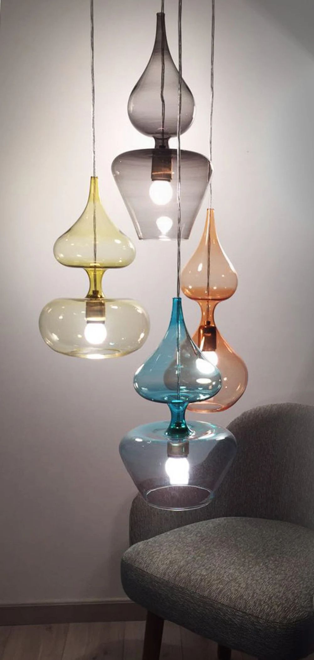 Colorful glass pendant lights hang above a chair against a plain wall.