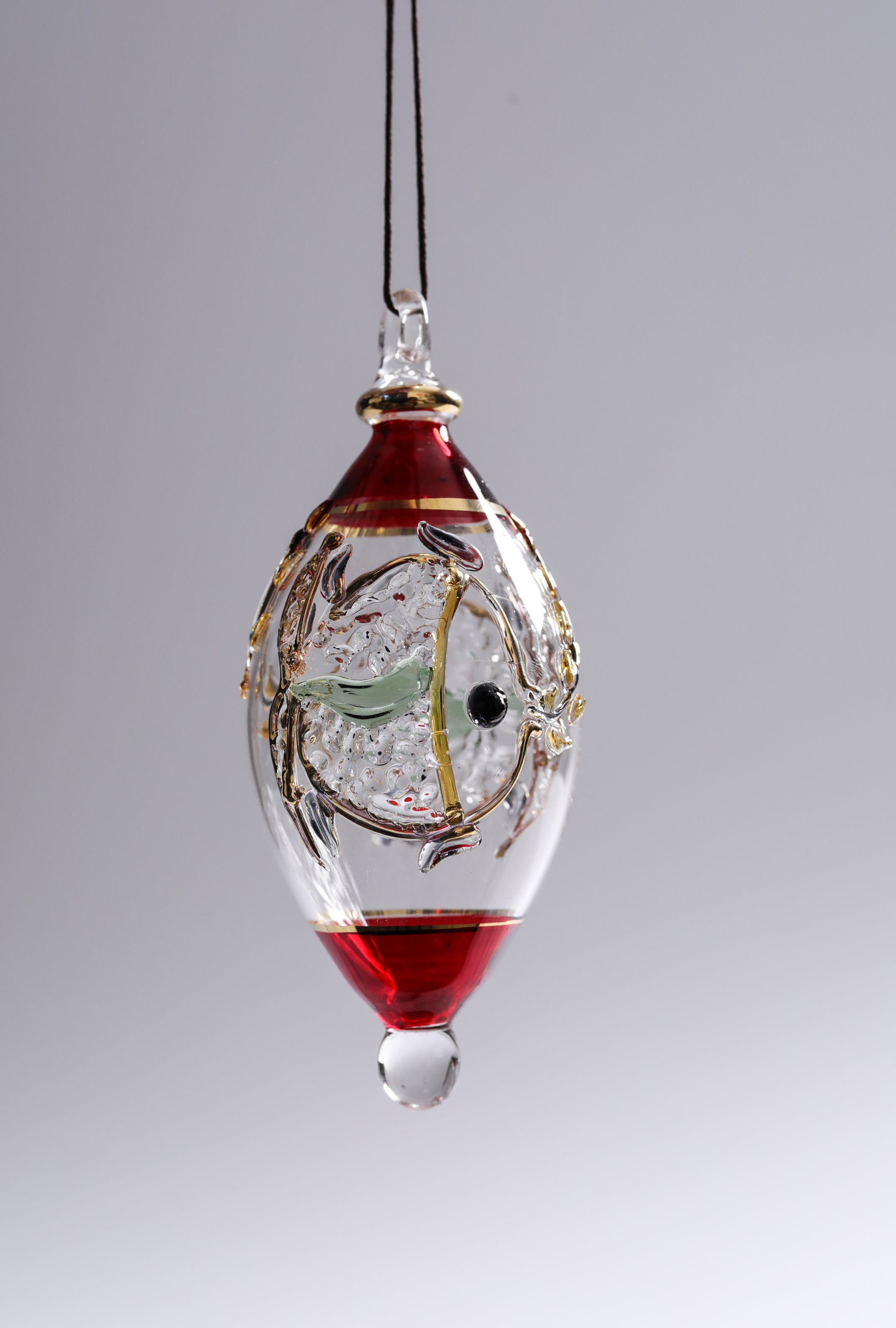 Decorative glass hanging ornament with red liquid and gold accents on a gray background