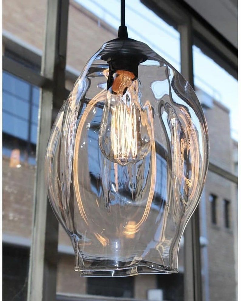 Clear glass pendant light with a visible bulb against a blurred window background