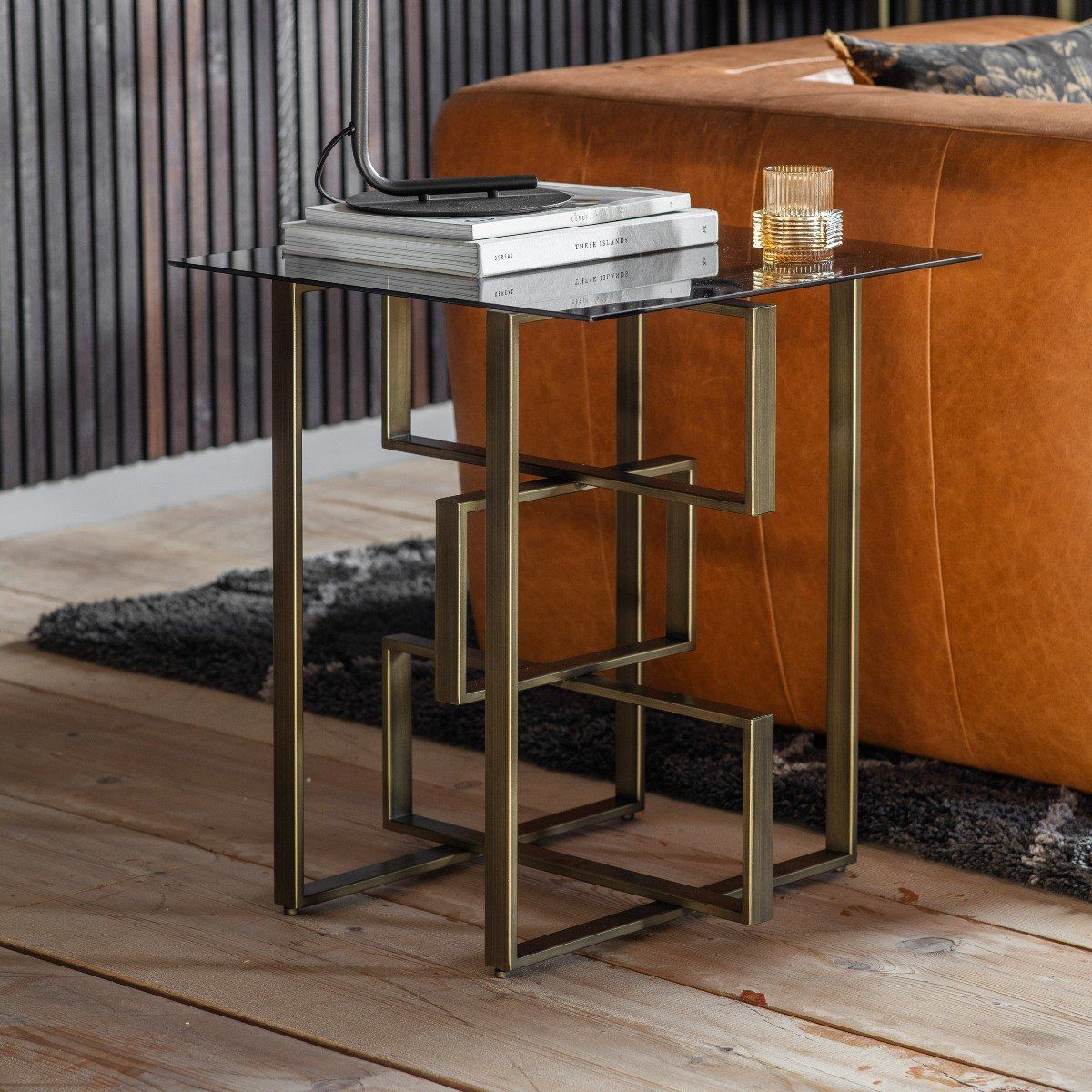 Modern side table with gold legs next to a brown sofa on a wooden floor.