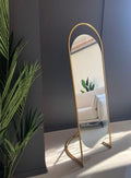 Gold standing mirror against a dark wall with a plant to the left