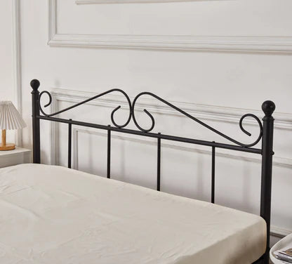 Black metal bed frame with decorative scrollwork against a white wall.