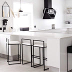 Modern kitchen with white countertops and black bar stools.