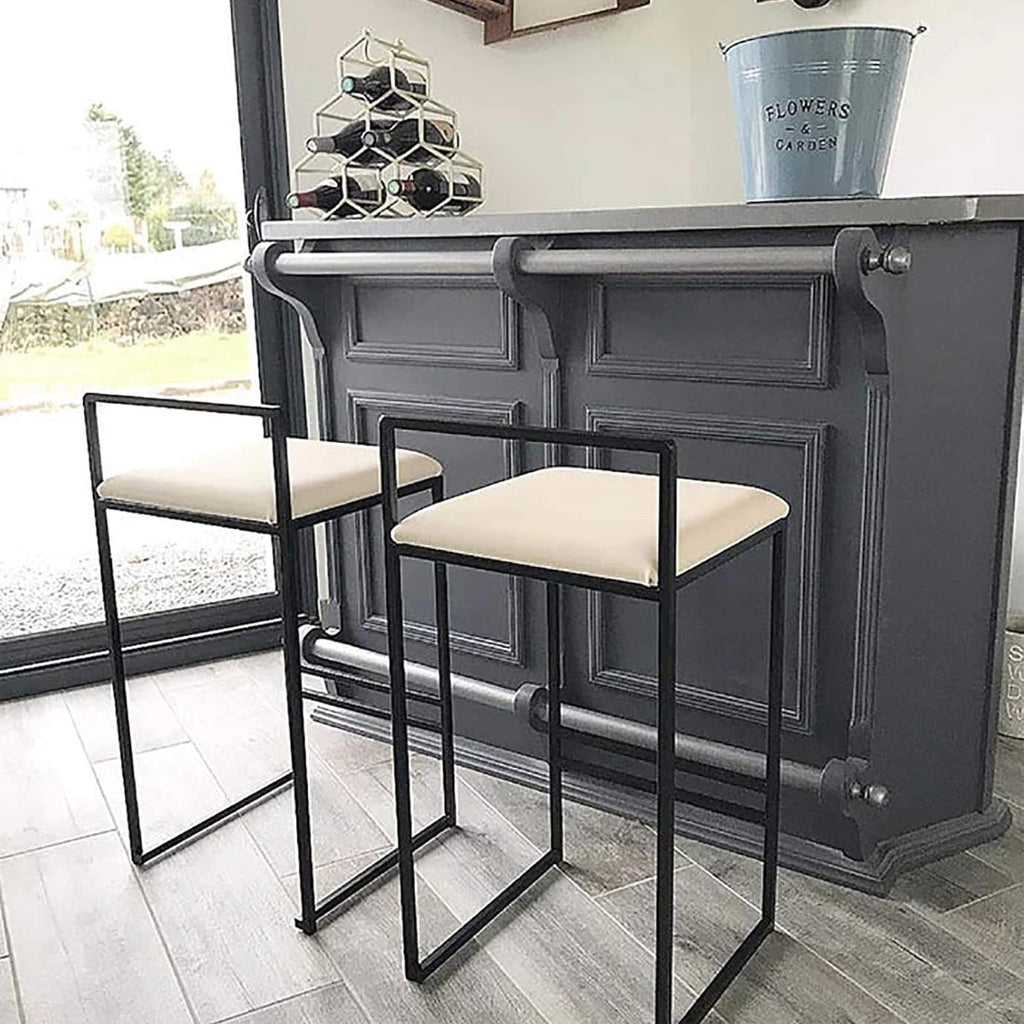 Two bar stools with black metal frames and beige cushioned seats in front of a dark gray bar.