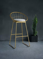 Gold metal bar stool with a gray cushion against a dark background