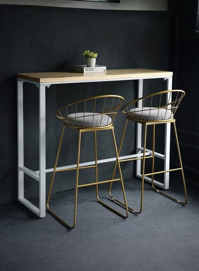 Two gold bar stools with white cushions in front of a wooden table against a dark wall.