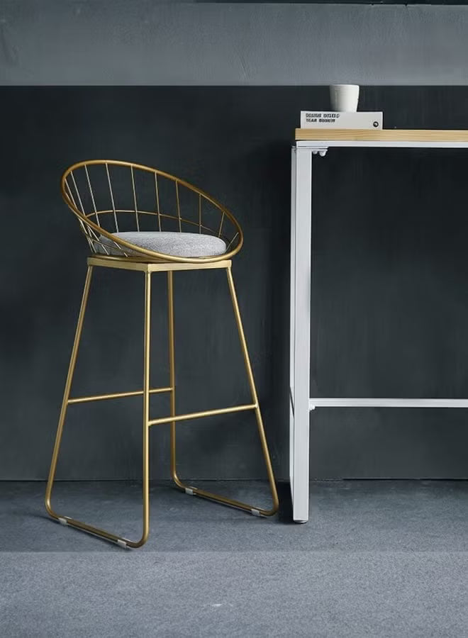 Gold bar stool with a gray cushion next to a white table against a dark wall.