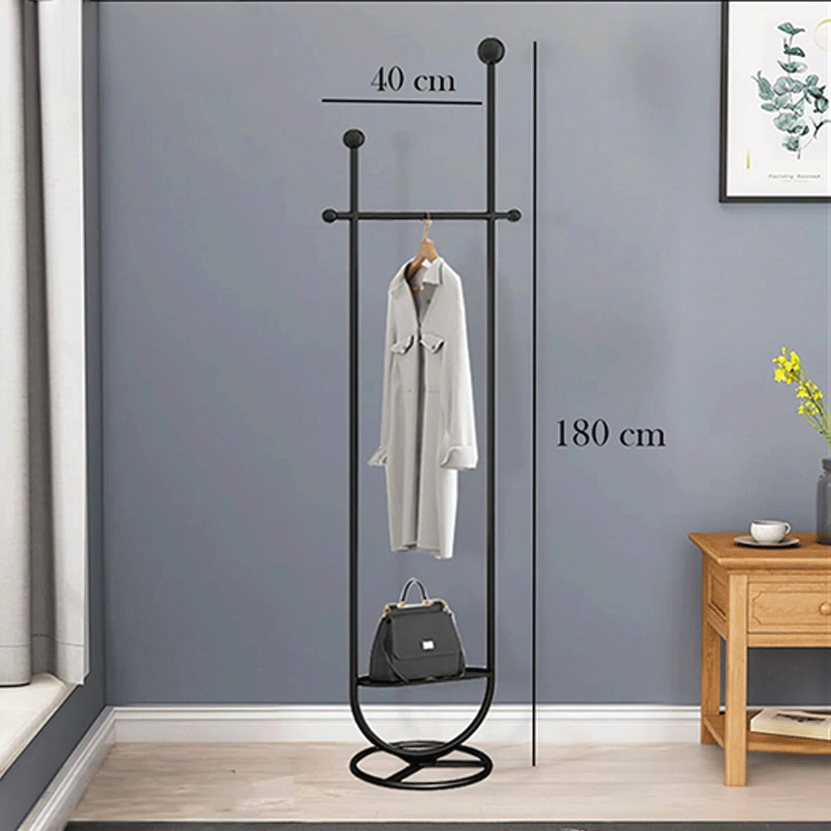 Black coat stand with measurements against a gray wall, featuring a white coat and black bag.
