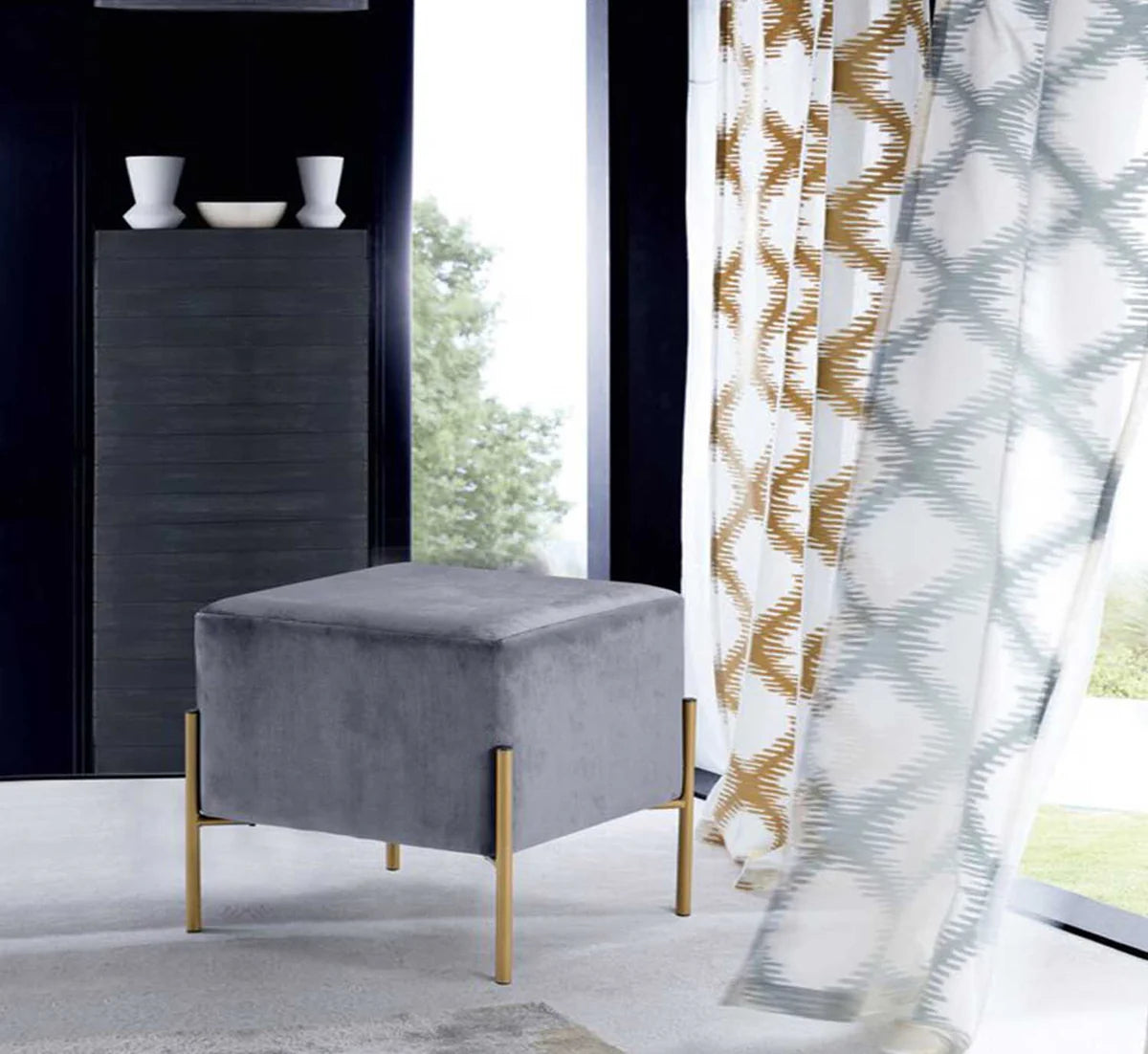 Gray ottoman with gold legs in a room with patterned curtains.