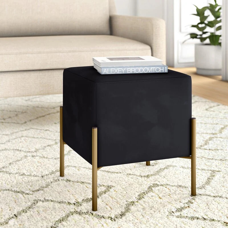 Black cube-shaped side table with gold legs in a living room setting.