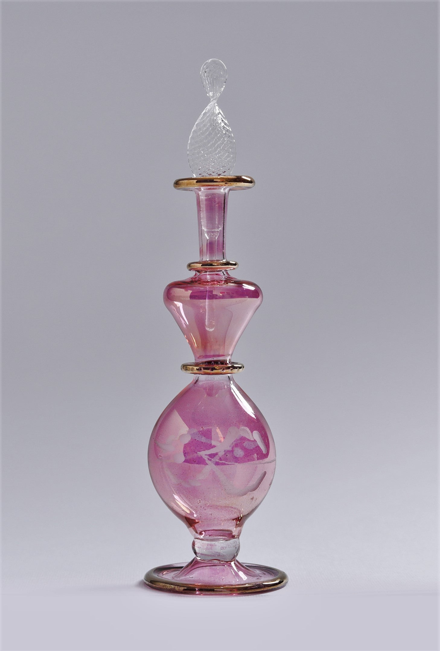 Pink glass perfume bottle with a decorative stopper on a gray background