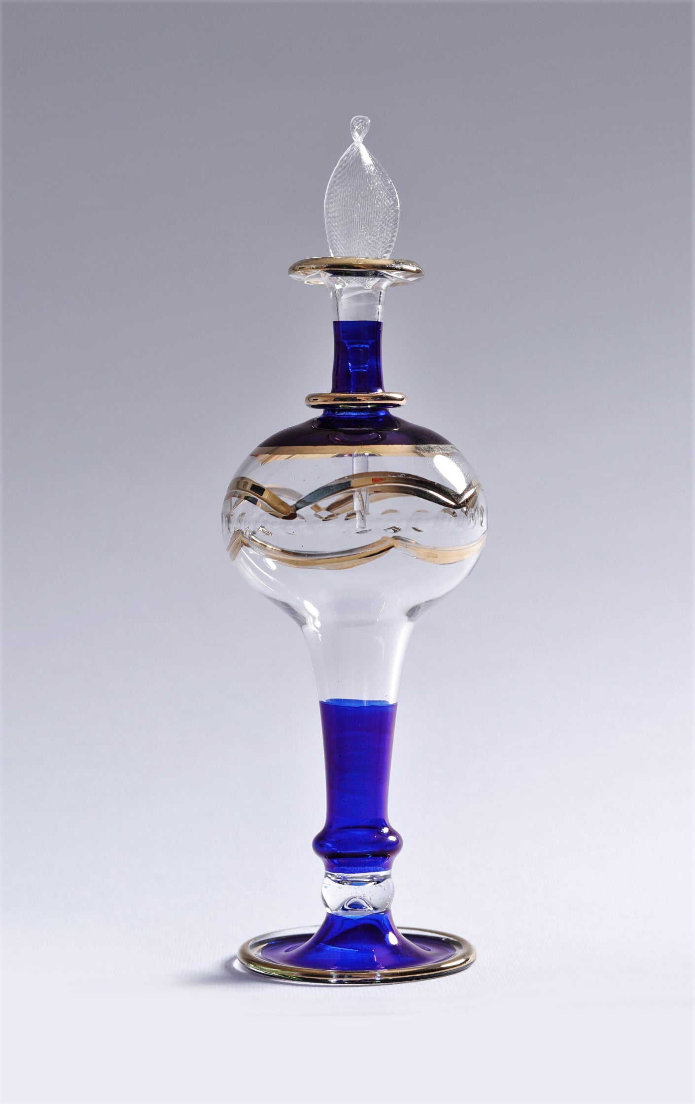 Glass decanter with blue base and gold accents on a gray background