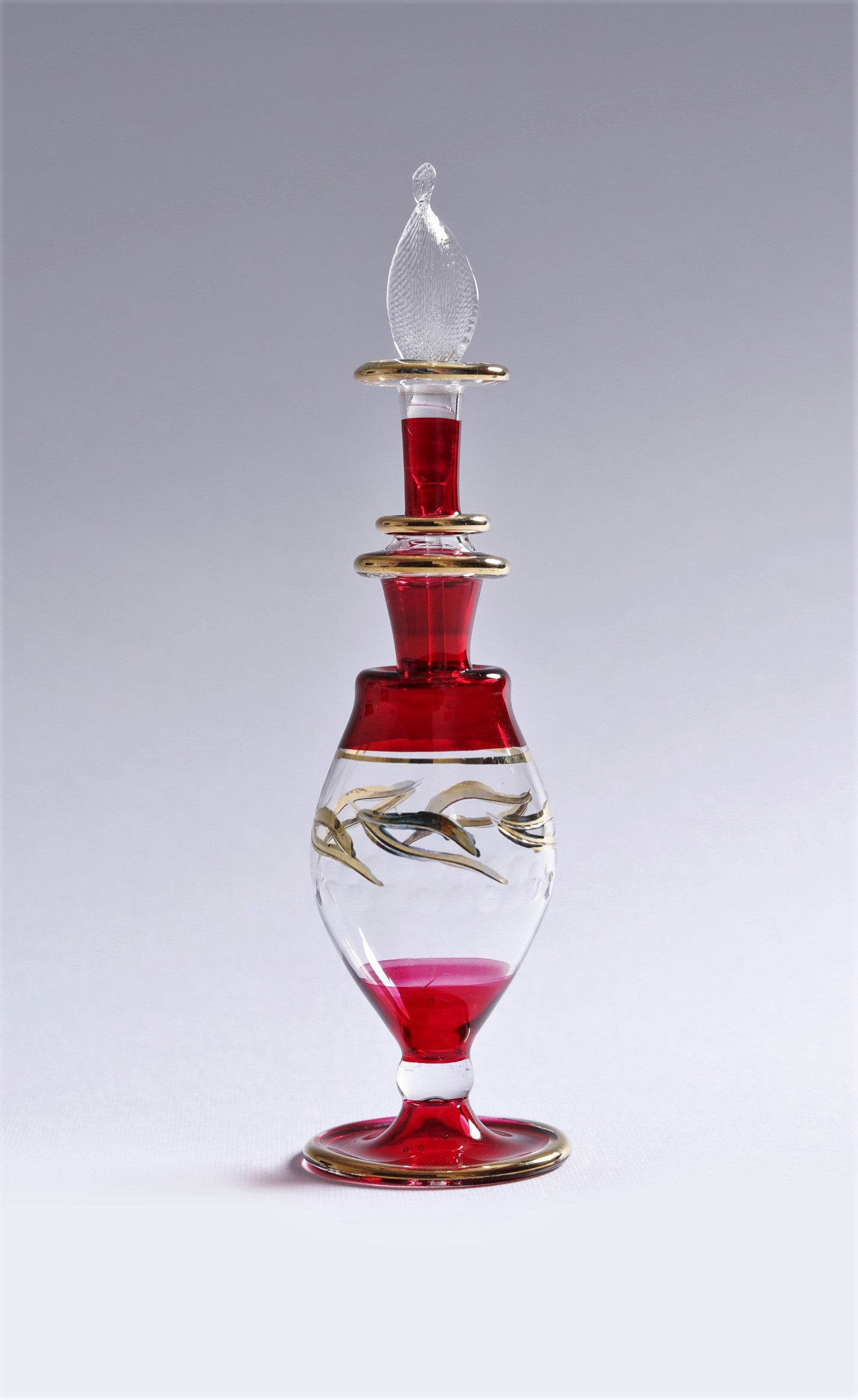 Decorative glass bottle with red liquid and gold accents on a gray background