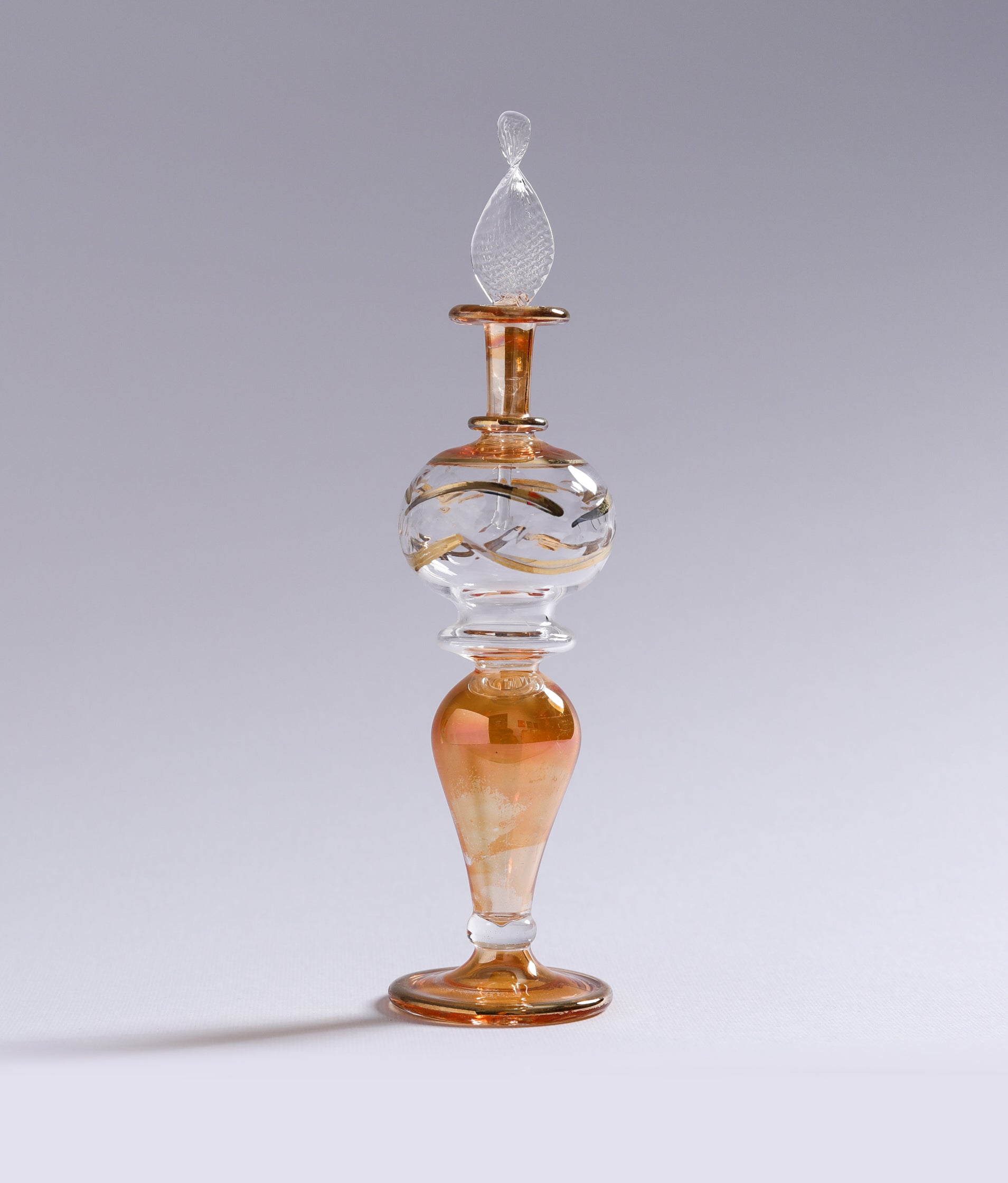 Decorative glass bottle with a gold base and intricate design on a gray background