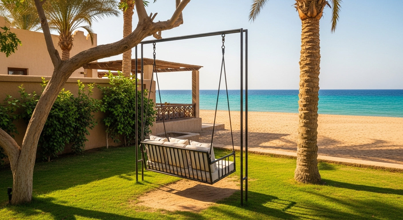 Swing set with cushions on a grassy area near a beach with palm trees and ocean view.