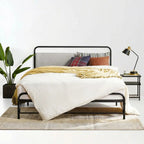 Bedroom with a bed featuring a black metal frame, white bedding, and colorful pillows, next to a nightstand with a lamp.