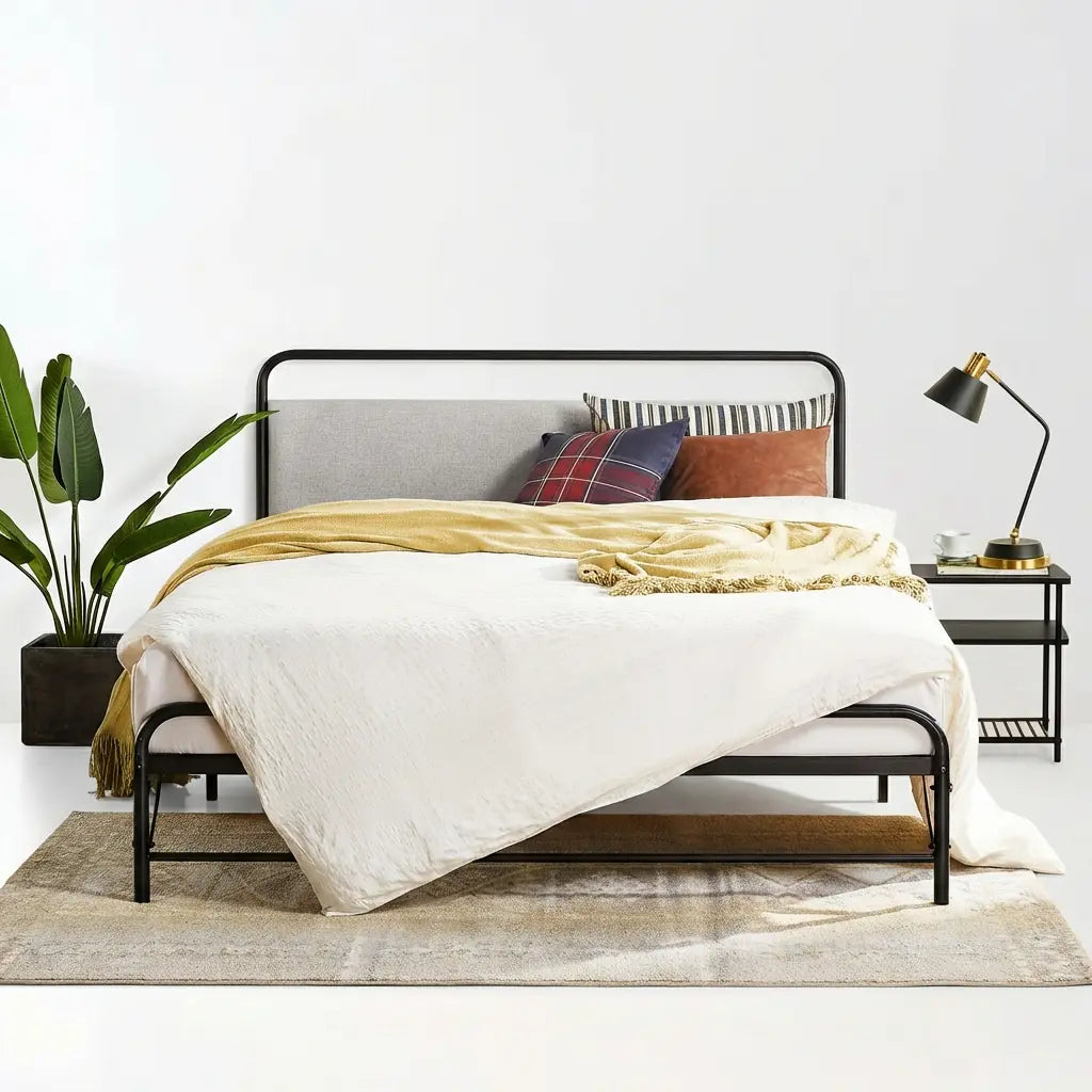 Bedroom with a bed featuring a black metal frame, white bedding, and colorful pillows, next to a nightstand with a lamp.